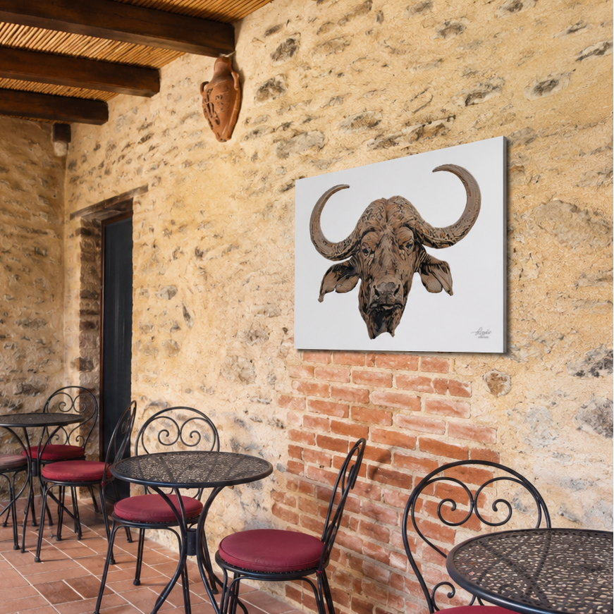A square canvas print of a detailed bull head artwork hanging on a rustic stone wall in an outdoor patio setting with metal tables and red cushioned chairs.